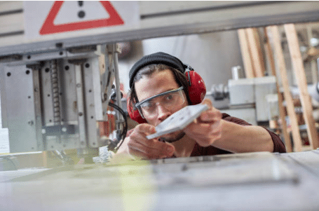 homme avec casque anti bruit qui regarde une pièce à côté d'une machine industrielle