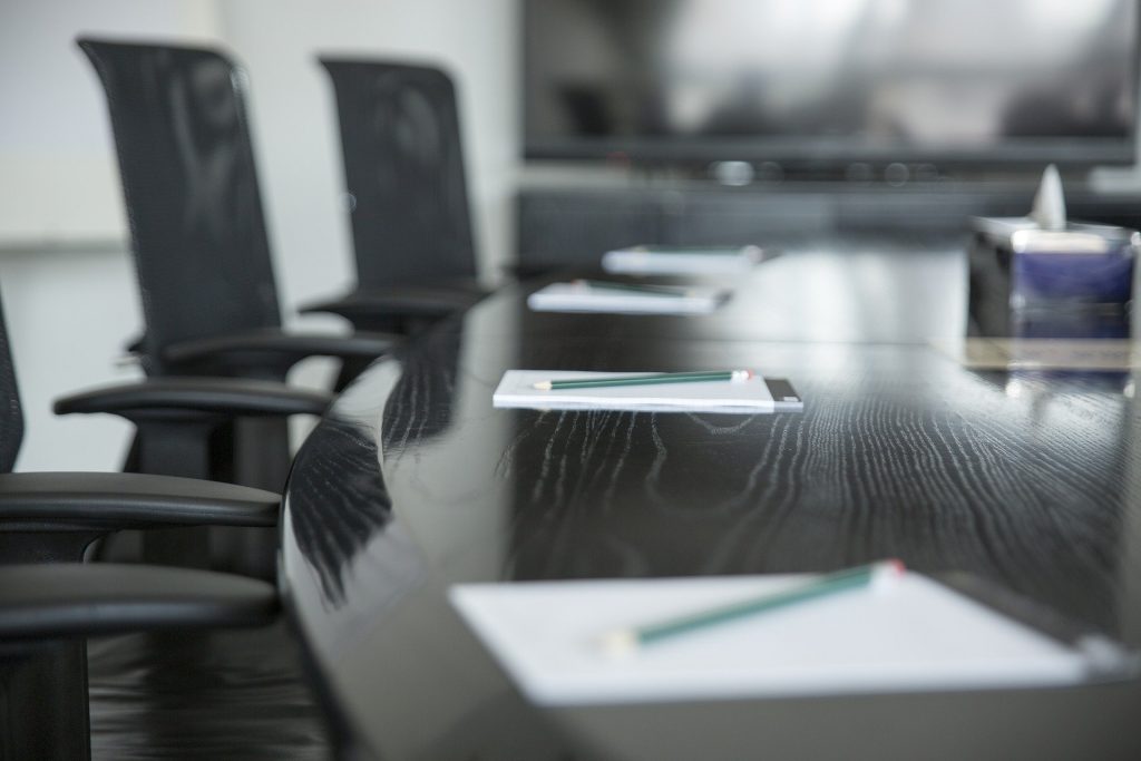 Salle de réunion avec une table au centre sur laquelle sont posés des carnets avec stylos à chaque place et des chaises de bureau autour